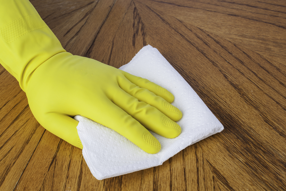 person cleaning wooden floor with paper towel wearing gloves