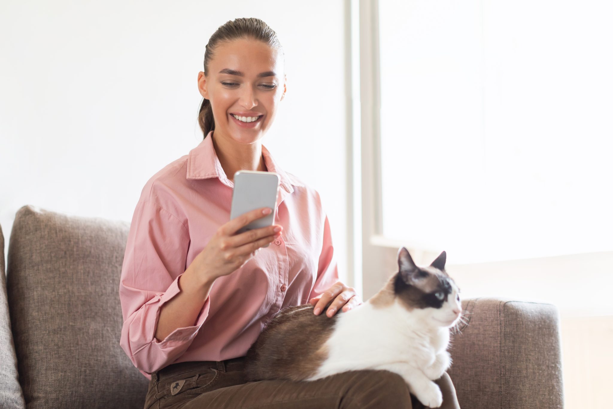 woman using her phone with a cat on her lap