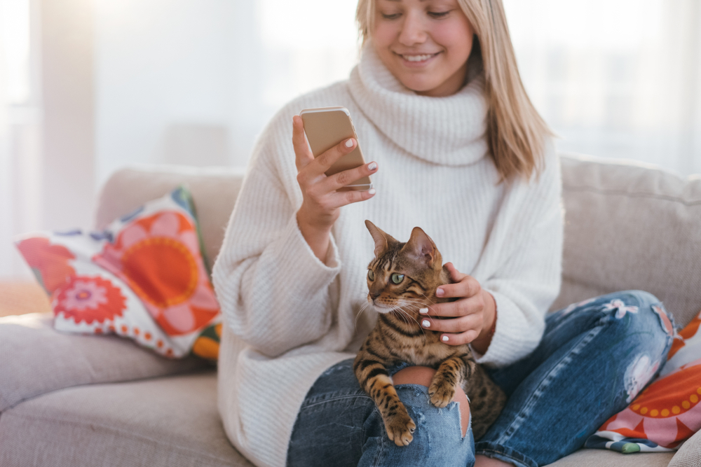 Mujer usando su teléfono con su gato en su regazo.